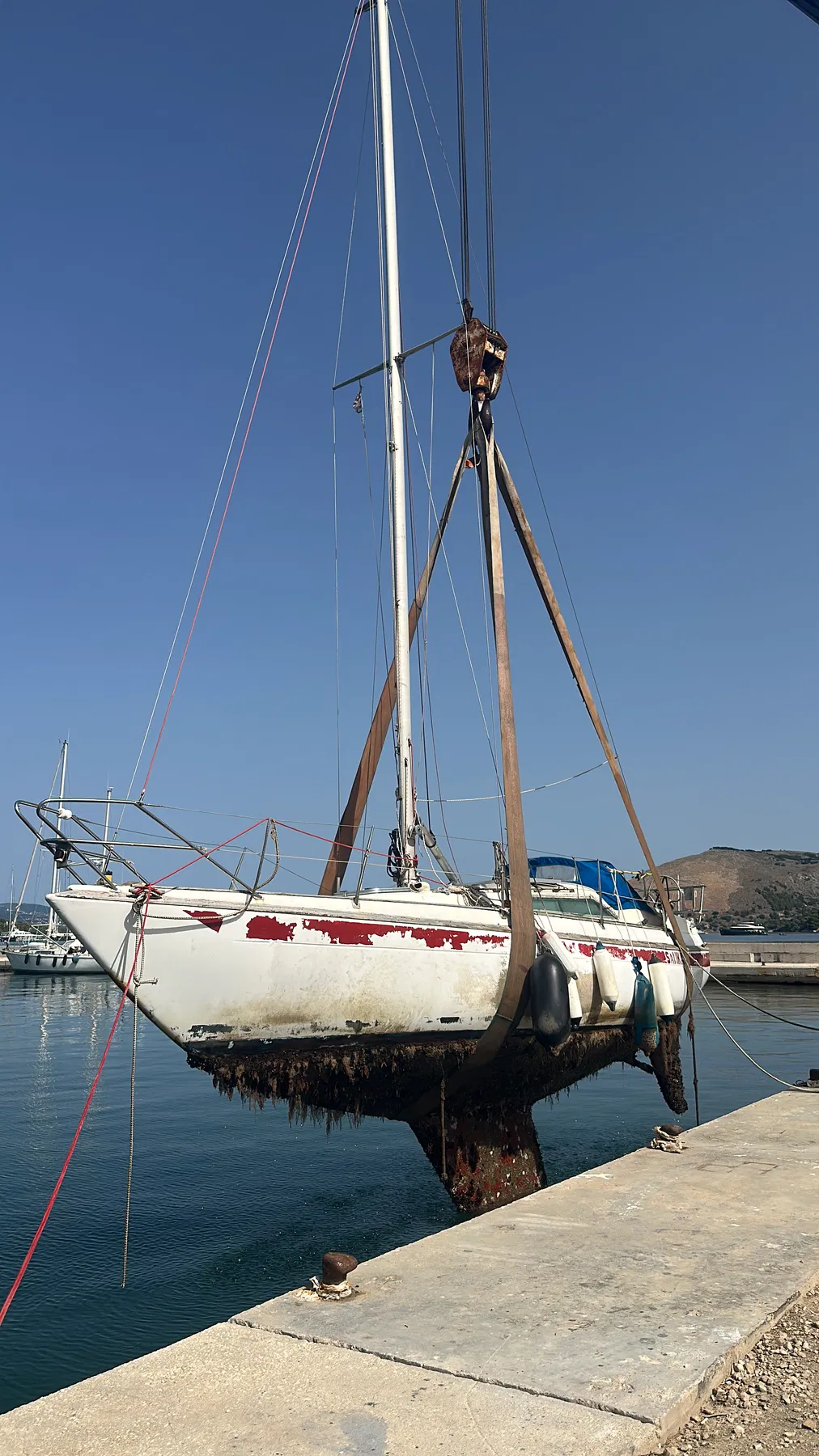 Geschädigtes Boot SANKARA – Seitenansicht an Land während der Auskran-Dokumentation; roter Rumpfstreifen und Unterwasserschiff sind sichtbar.